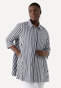 Camicia a righe nei toni del blu e del bianco, con maniche a tre quarti, colletto e una vestibilità rilassata con aperture laterali per una maggiore libertà di movimento.