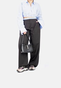 Camisa corta de color azul claro, pantalones negros de pierna ancha, bolso negro con herrajes plateados y zapatillas deportivas multicolor de suela gruesa.