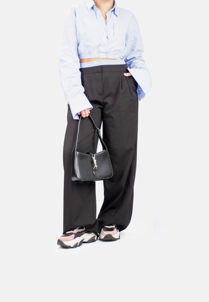 Camisa corta de color azul claro, pantalones negros de pierna ancha, bolso negro con herrajes plateados y zapatillas deportivas multicolor de suela gruesa.