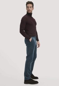 Dunkler Rollkragenpullover, blaue Cordhosen und schwarze Wildlederschuhe. Moderner Schnitt, strukturierter Stoff und Seitentaschen.