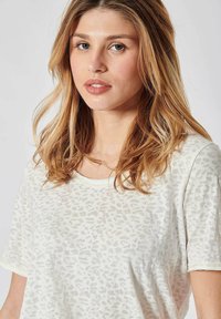 T-shirt blanc avec un motif léopard subtil, manches courtes et col arrondi. Texture douce avec des coutures accentuées en jaune.