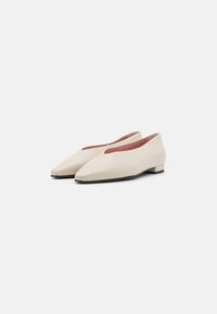Scarpe piatte beige con design a punta, superficie liscia, tacco basso a blocco e un sottile dettaglio a taglio sulla parte superiore. Suola nera.