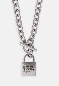 Srebrna metalna ogrlica s lancem koja sadrži prevelike karike, zatvarač na preklop i kvadratni privjesak ugraviran s "Don Ed Hardy dizajni."