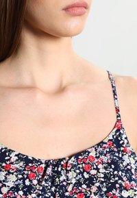 Haut à imprimé floral avec fines bretelles, présentant une base bleu marine foncé et de petites fleurs roses et blanches ; tissu léger à la texture douce.