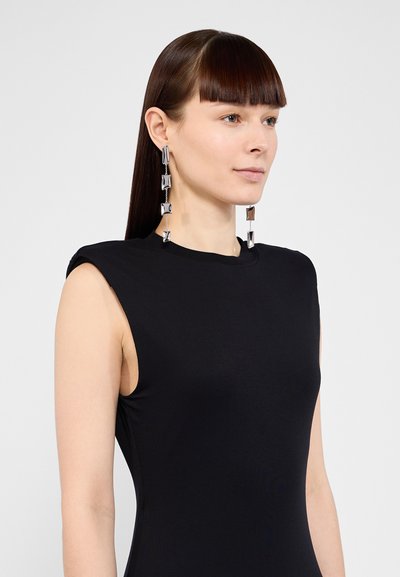 Black sleeveless top with a fitted design. Features long, shiny silver earrings with geometric shapes, enhancing contemporary aesthetics.