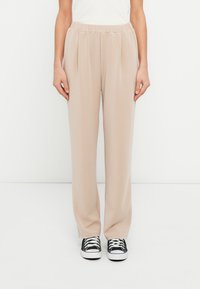 Μπεζ, ψηλόμεσο παντελόνι με φαρδύ πόδι, κατασκευασμένο από απαλό ύφασμα με πιέτες. Συνδυασμένο με μαύρα αθλητικά παπούτσια με λευκές λεπτομέρειες.