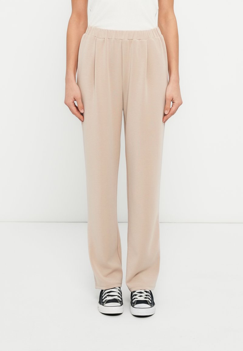 Μπεζ, ψηλόμεσο παντελόνι με φαρδύ πόδι, κατασκευασμένο από απαλό ύφασμα με πιέτες. Συνδυασμένο με μαύρα αθλητικά παπούτσια με λευκές λεπτομέρειες.