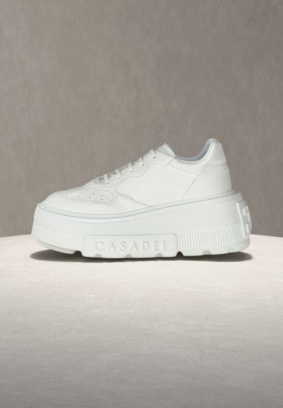 Baskets à plateforme blanches avec un design à lacets et une semelle épaisse texturée embossée du mot "CASADEI", présentées sur une surface claire contre un fond neutre.