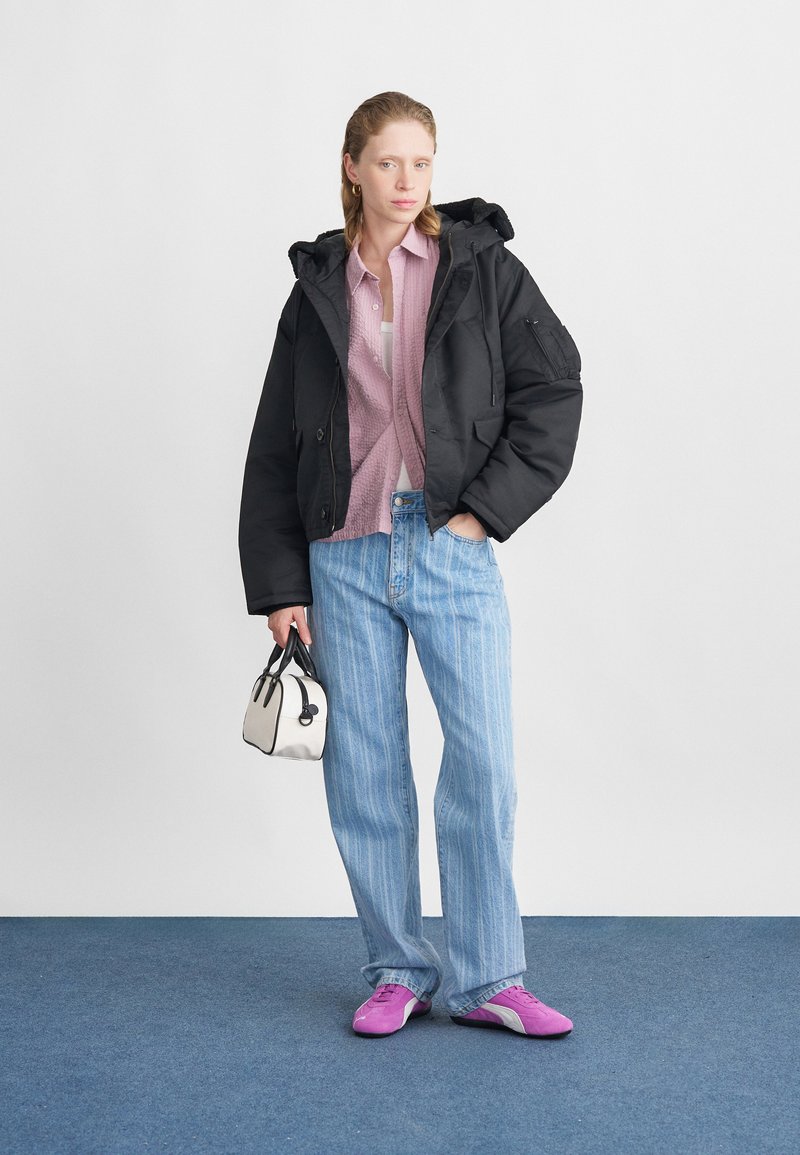 Schwarz isolierte Jacke, hellrosa Hemd, blau gestreifte Jeans, kleine weiße Handtasche und lila Sneakers mit niedrigem Schnitt. Einfaches, lässiges Ensemble.