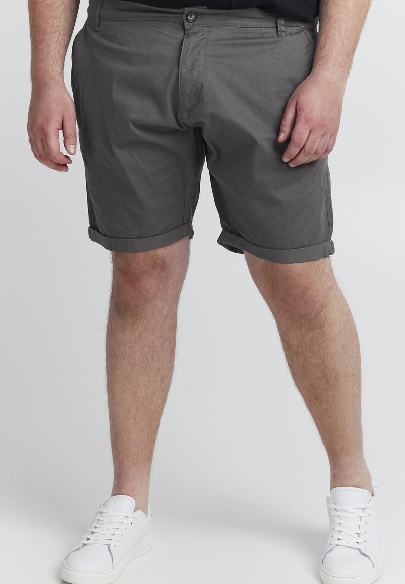 Pantalones cortos de algodón grises con dobladillo enrollado, bolsillo frontal y cierre de botón. Se llevan con zapatillas blancas para un look casual.