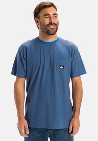 Modrý pruhovaný tričko s kulatým výstřihem a kapsou na hrudi, vyrobené z bavlny. Obsahuje logo na kapse a kontrastní manžety.
