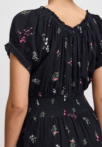 Robe en tissu noir avec des motifs floraux en rose, blanc et vert ; présente une taille smockée et un décolleté froncé avec des manches courtes.