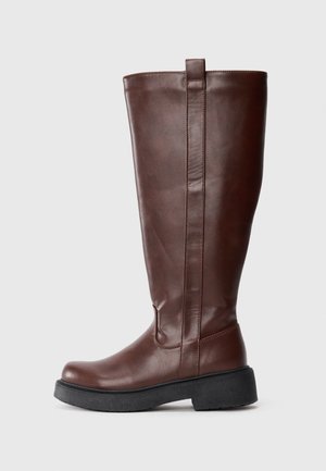 Brown leather knee-high boots with a slightly rounded toe, textured finish, and a thick black rubber sole. Features a pull tab at the top.