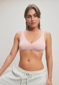 Bralette wireless rosa con scollatura a V, spalline sottili, design senza cuciture e materiale morbido e elastico. Abbinato a pantaloni tuta grigi con cordino.