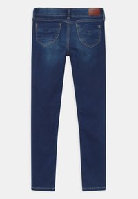 Jeans ajustados de denim en azul oscuro, con un parche en la cinturilla trasera, dos bolsillos traseros con sutiles detalles de costura y una textura suave.