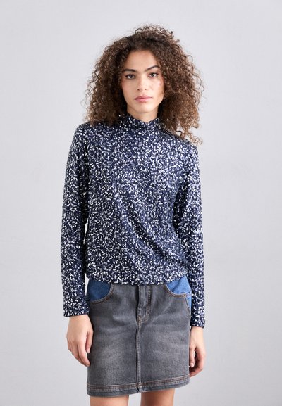 Blusa de manga larga azul marino con un patrón floral blanco, cuello alto. Combinada con una falda de mezclilla gris que presenta bolsillos de mezclilla azul.
