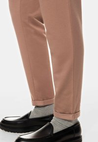 Pantalons en coton rose à forme fuselée avec des revers, associés à des mocassins noirs et des chaussettes gris clair.
