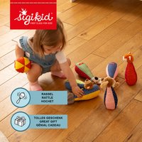 Colorful children's toys on wooden floor: a striped rattle in bright colors, soft animal figures, and a child reaching for them.
