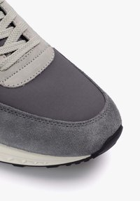 Adidași gri cu un amestec de materiale fine și de piele suede, cu cusături proeminente, șireturi plate și o talpă texturată din cauciuc negru.