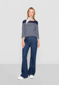 Jūrų kariuomenės ir baltos juostelės ilgomis rankovėmis viršus, derinamas su tamsiai mėlynomis plačiomis džinsais. Modelis dėvi baltus sportbačius ir baltą kaklo šalį.