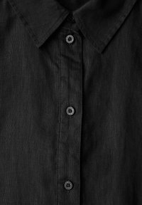 Camisa de lino negra con un cuello clásico, tapeta de botones en la parte delantera con botones negros y un acabado de tela texturizada.