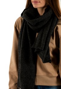 Bufanda gris oscuro hecha de un tejido suave y texturizado, llevada de manera suelta alrededor del cuello, combinada con una sudadera beige en un entorno casual.