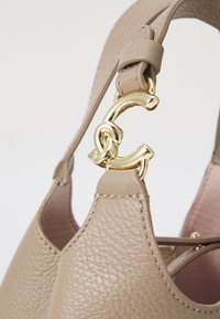 Beige leather handbag with textured surface, featuring a gold hardware accent shaped like a letter "C" on the strap.