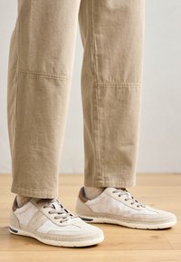 Beige sportcipők vegyes anyagú panelekkel, kerek orral, fűzős kialakítással és gumitalppal. Világos színű vászon és nubuk díszítések.