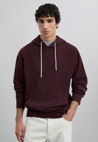 Sudadera color burdeos con capucha ajustable, bolsillo tipo canguro en la parte delantera y puños acanalados. Fabricada en un tejido suave de mezcla de algodón con una textura sutil.