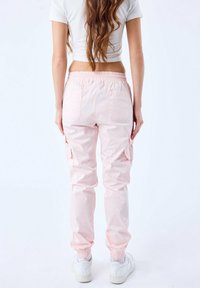 Helle rosa Cargo-Hosen mit einem elastischen Bund, seitlichen Taschen und zulaufenden Bündchen, aus einem glatten Stoff gefertigt. Keine sichtbaren Muster.