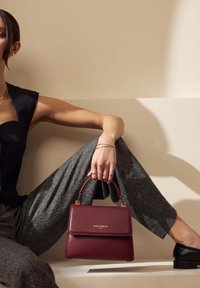 sac à main en cuir bordeaux avec un design structuré, une anse supérieure et des accents en métal doré, placé sur un fond neutre.