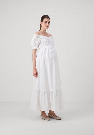 Biele off-shoulder šaty s puff rukávmi a volánom. Hladká bavlnená tkanina, priliehajúci korzet, nosené s béžovými ozdobenými balerínami.