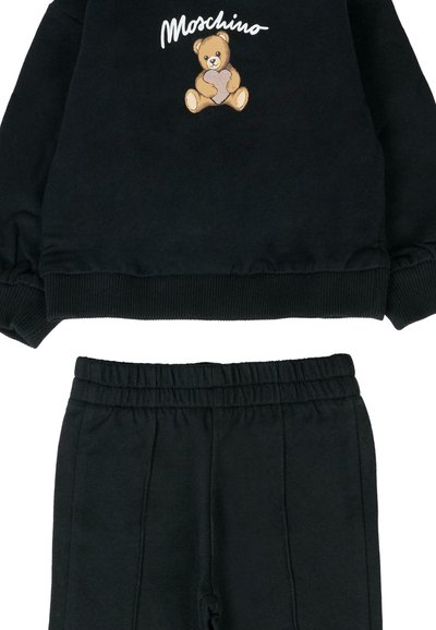 Czarny zestaw składający się z bluzy i spodni, z grafiką niedźwiedzia i napisem "Moschino". Bluza ma ściągacze przy rękawach; spodnie mają elastyczny pas.