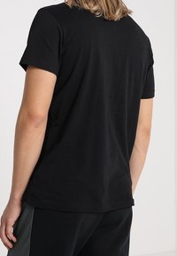 Mustat puuvillaa t-paita, jossa on lyhyet hihat ja pyöreä kaula-aukko. Sujuva pinta, suora helma, ei näkyviä logoja tai kuoseja. Rentoa istuvuutta.