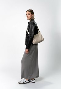 Giacca di pelle nera, gonna grigia lunga, sneakers bianche e nere. Borsa a spalla beige chiaro con tracolla regolabile. Orecchini a perno semplici.