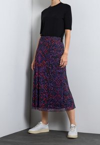 Svart kortärmad topp kombinerad med en flödande, mönstrad maxikjol i lila, röd och svart, kompletterad med vita sneakers.