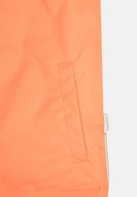 Ryškiai oranžinė audinio medžiaga su lygiu paviršiumi, turinti šoninę kišenę ir prekės ženklo etiketę su užrašu „Huppa“ krašte.