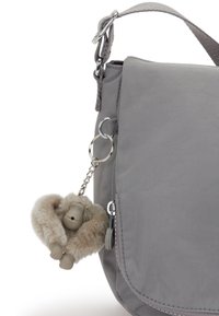 Graue Stoff-Crossbody-Tasche mit einem Deckel, die mit einem plüschigen Anhänger in Form eines Affen an einem silbernen Schlüsselring versehen ist.