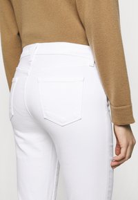 Jeans blancos hechos de denim con una textura suave. Las características incluyen bolsillos traseros, una cintura alta y una forma ajustada.