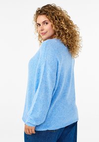 Hellblau gestrickter Pullover mit lässiger Passform, überschnittenen Schultern und gerippten Bündchen, kombiniert mit dunkelblauen Jeans. Strukturierter Stoff.