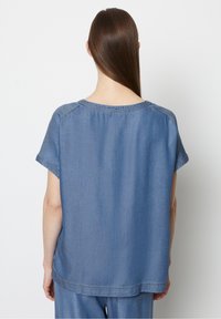 Top in denim azzurro chiaro con maniche corte, scollatura rotonda e vestibilità rilassata. Presenta una texture morbida e una delicata cucitura lungo i bordi.