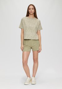 Jasnozielona koszulka z krótkim rękawem w białe kropki, zestawiona z beżowymi szortami. Model nosi off-white trampki. Prosty, casualowy design.