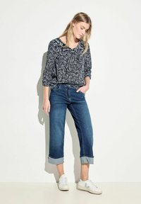 Blusa a motivi paisley in bianco e nero, maniche tre quarti, abbinata a jeans blu scuro arrotolati e sneakers bianche.