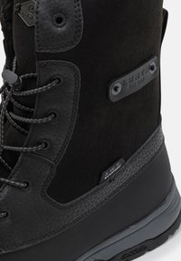 Musta vedenpitävä saapas, jossa on teksturoidusta nahasta valmistettu päällinen, kestävät nauhat, kohokuvioitu brändäys ja kumipohja, jossa on kuvioitu pito.