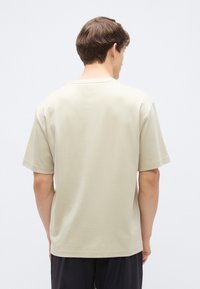 Jasnobeżowy t-shirt z krótkim rękawem wykonany z gładkiej bawełny, z okrągłym dekoltem i luźnym krojem, z gładkim tyłem bez widocznych wzorów.