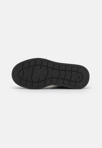 Black rubber shoe sole with a textured tread pattern, featuring grooves and ridges for traction and durability.