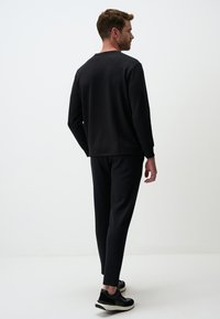 Completo sportivo nero composto da una maglietta a maniche lunghe e pantaloni affusolati, realizzato in tessuto liscio; include polsini a coste e una texture sottile.