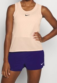 Canotta in rete rosa con scollo rotondo e logo Nike nero, abbinata a pantaloni shorts viola con un piccolo logo Nike bianco.