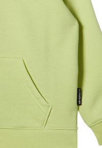 Limoengroene sweatshirt van zacht materiaal, met een kangoeroezak, geribbelde zoom en een klein merklabel aan de zijkant.