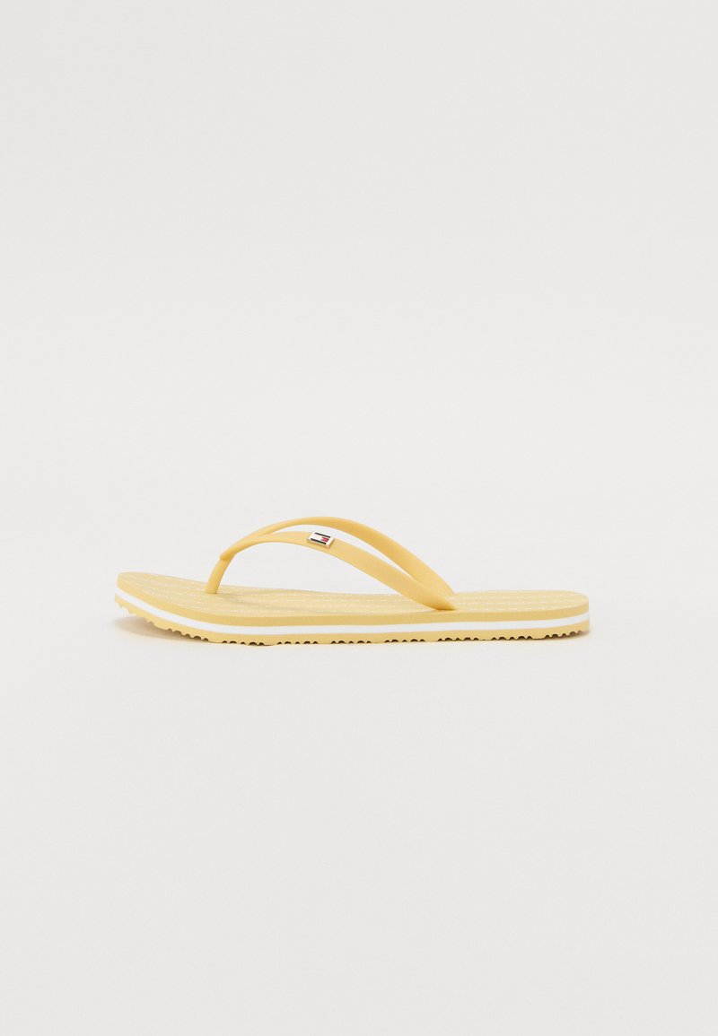 Tongs en caoutchouc jaune avec une semelle plate, dotées de deux fines lanières et d'un semelle texturée. Accent de logo notable sur une lanière.
